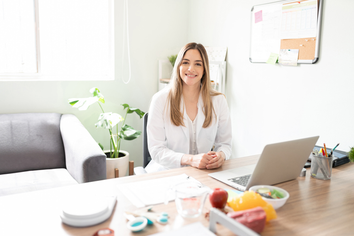 Registered Dietitian Nutritionist smiles in front of computer.