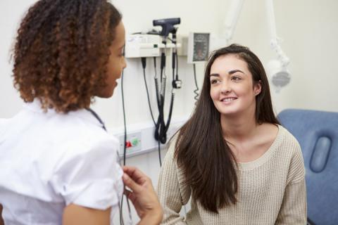 Young woman converses with nurse in clinic exam room.